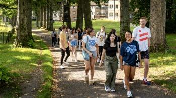 Students walking and talking as a group on a path on a shaded campus.