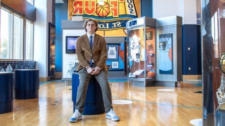 Connor Kerr posing in front of sports memorabilia wearing a dark tan suit.